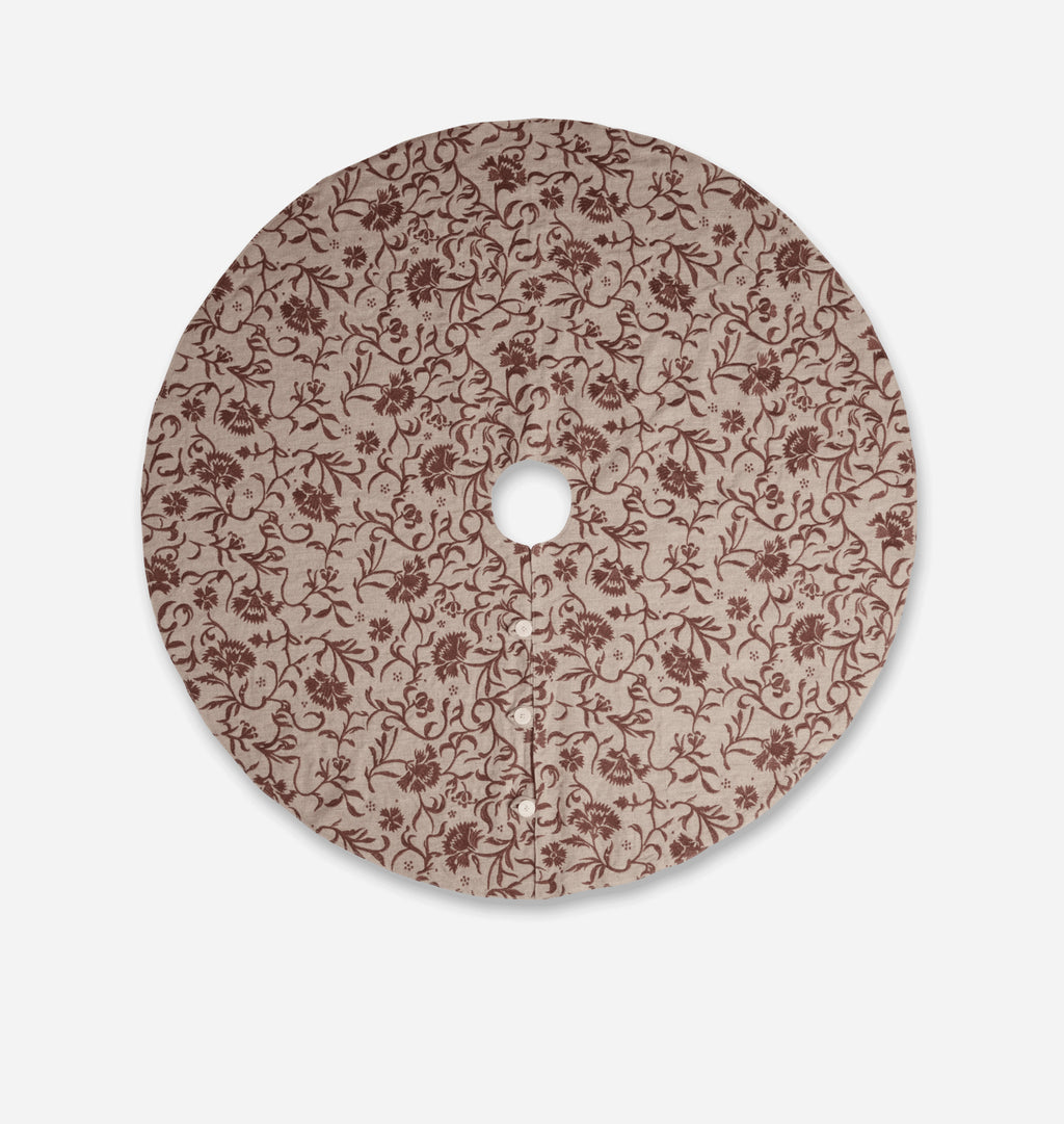 A round decorative tree skirt featuring an all-over floral vine pattern in dark brown on a warm beige background, shown against a light gray studio background.