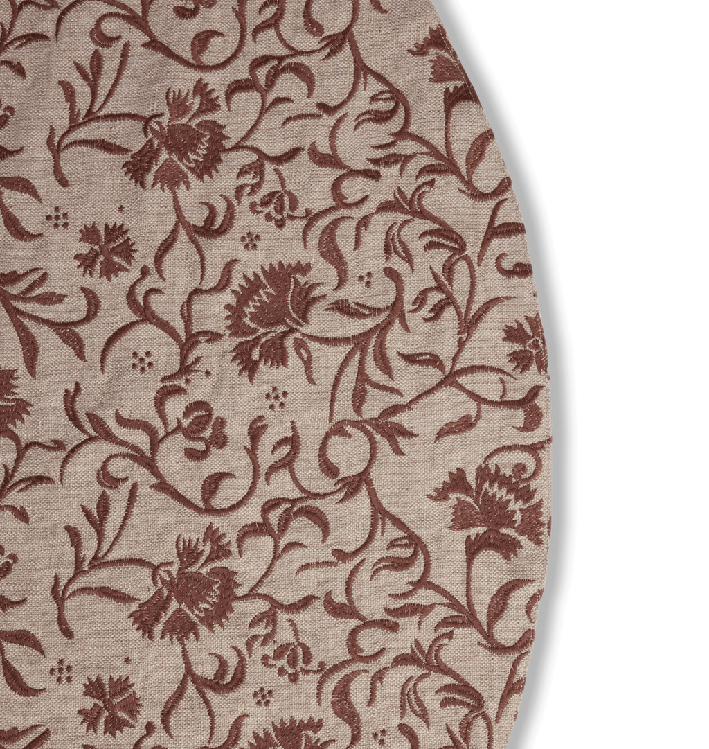 A round beige tree skirt with a reddish brown embroidered floral and scroll motif pattern with three button closures set against a white background