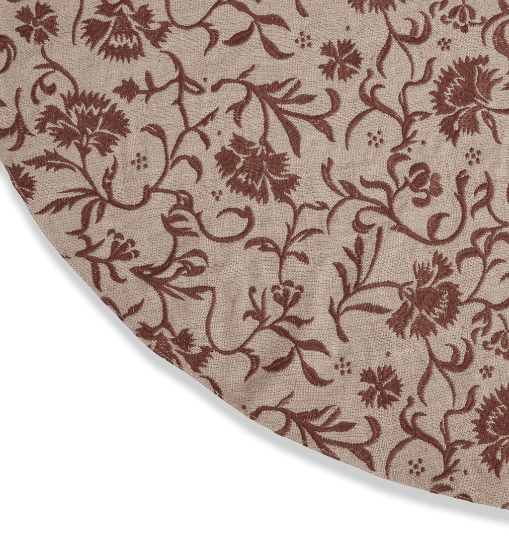 A round beige tree skirt with a reddish brown embroidered floral and scroll motif pattern with three button closures set against a white background
