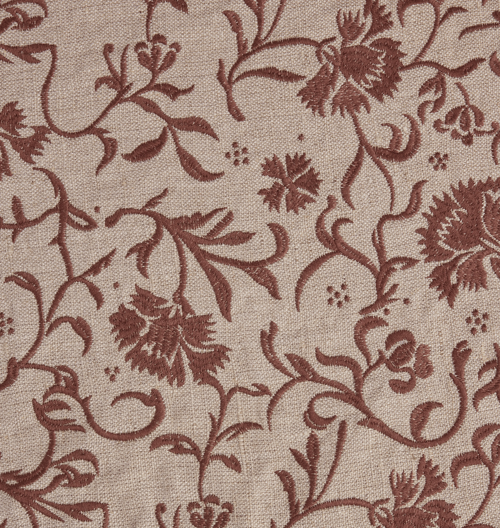 A close up fabric detail shot of a beige tree skirt with a reddish brown embroidered floral and scroll motif pattern 