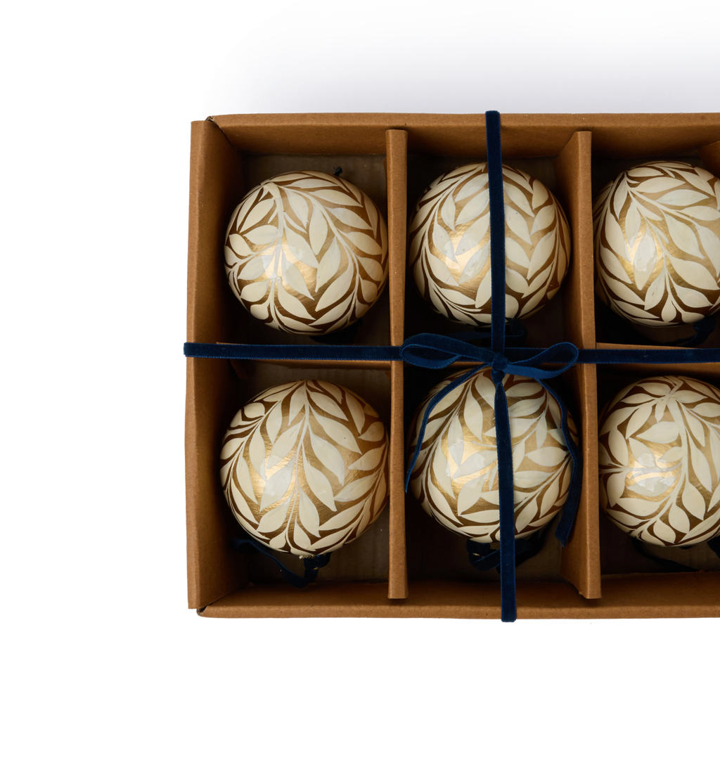 A set of decorative paper mache ornaments with gold floral patterns and blue velvet ties in a gift box