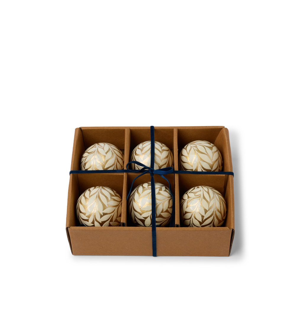 A set of decorative paper mache ornaments with gold floral patterns and blue velvet ties in a gift box