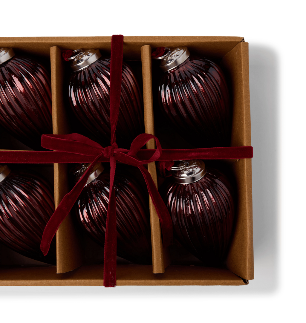 A gift set of brown glass ribbed ornaments in a cardboard box tied with a red velvet ribbon bow