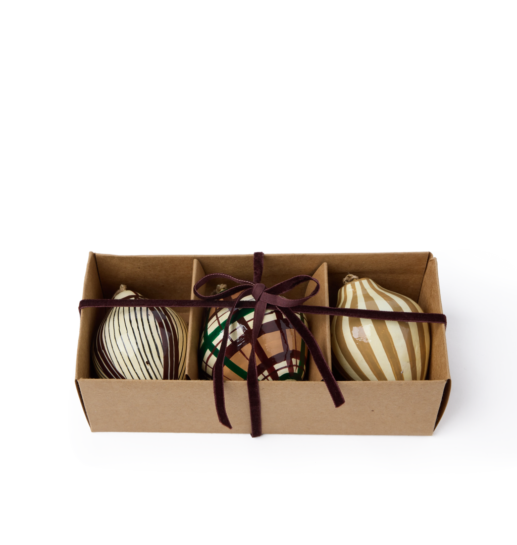 A set of decorative paper mache ornaments with striped and plaid patterns and red velvet ribbon in a gift box