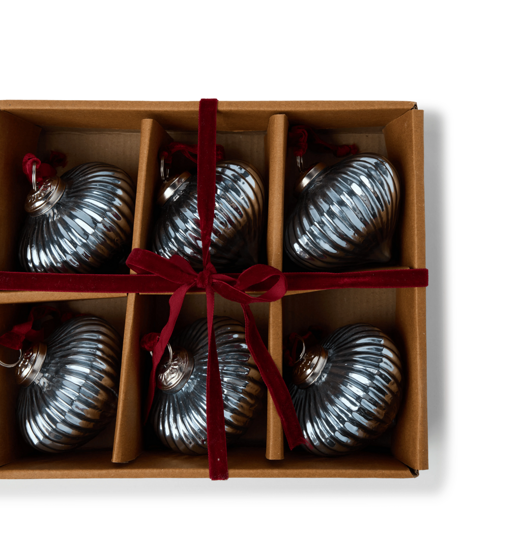 A gift set of light blue glass ribbed ornaments in a cardboard box tied with a red velvet ribbon bow