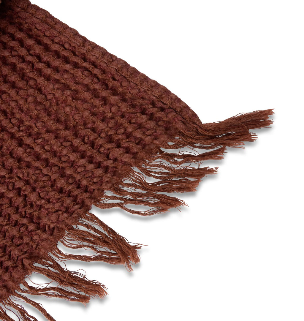 A detailed close up of the fringed edge of a warm red rust waffle weave blanket 