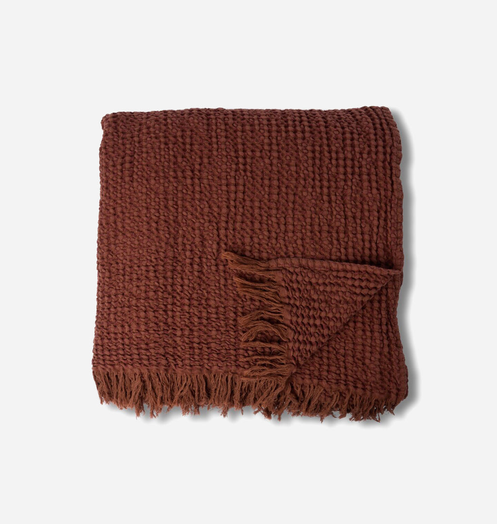 A overhead view of a warm rust colored waffle weave blanket with fringe edge shown on a white background