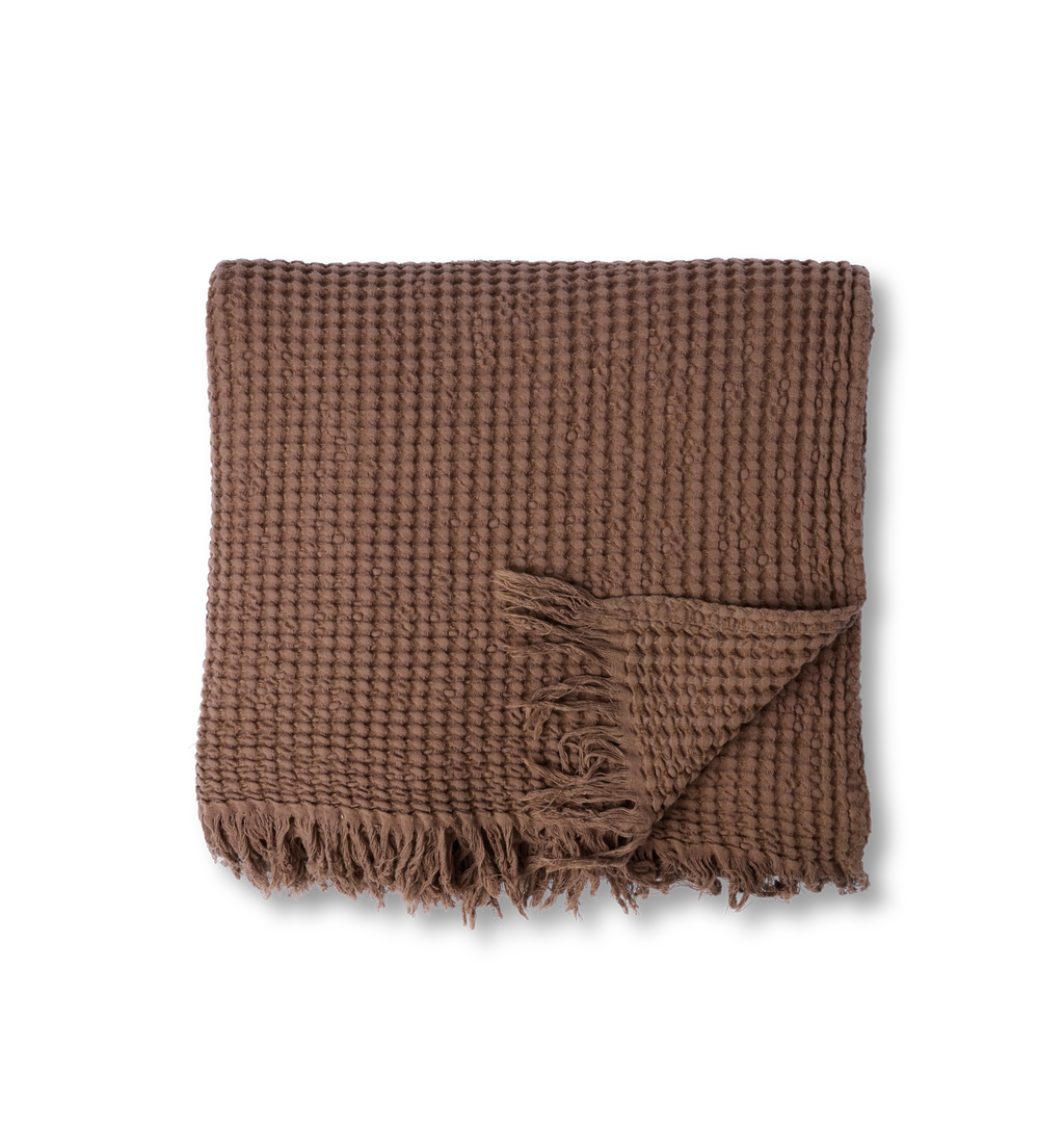 A overhead view of a light brown waffle weave blanket with fringe edge shown on a white background