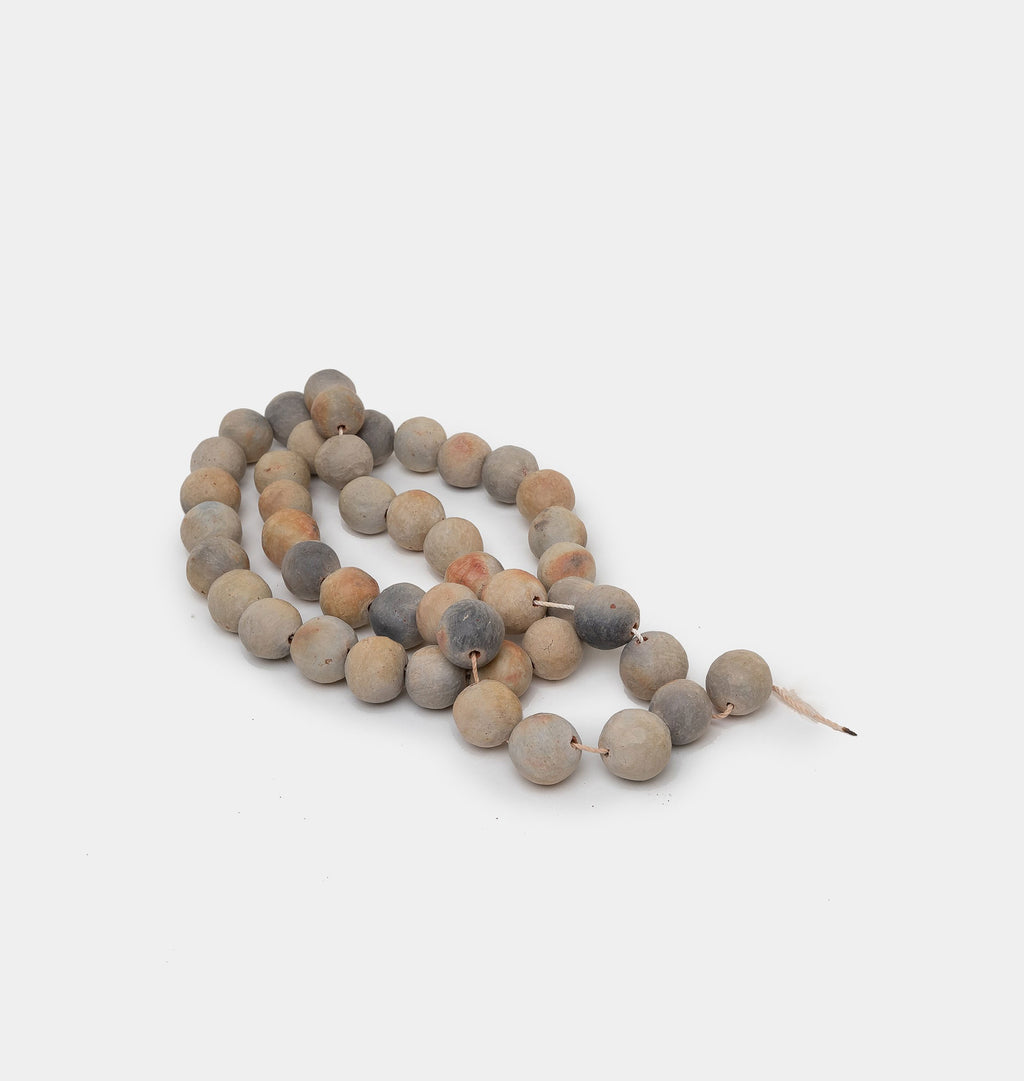 Decorative ceramic beads in grey and natural hues on a twine string set against a white background 