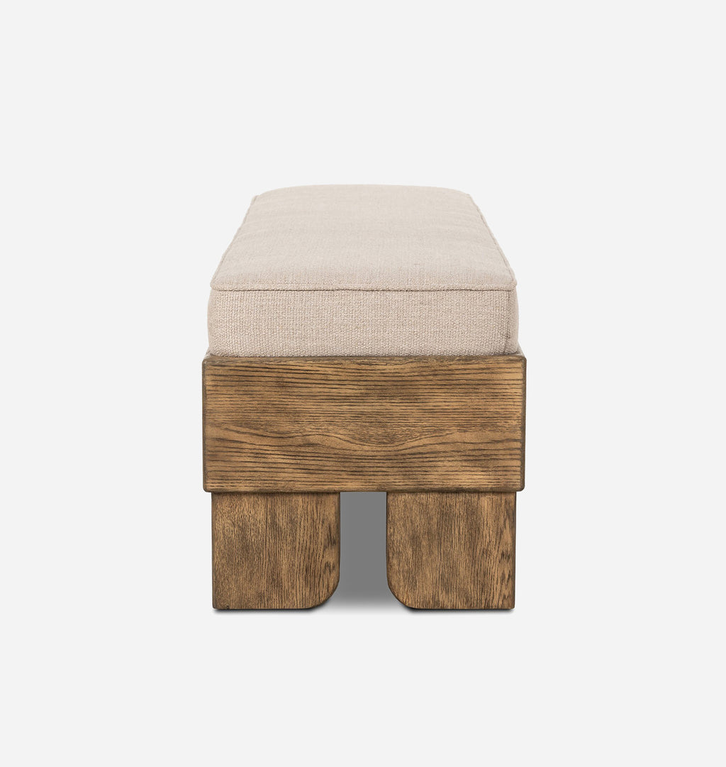 A modern bench with a thick, square beige upholstered cushion on top of a rustic, blocky medium-brown wooden base with integrated legs, shown against a plain white background.