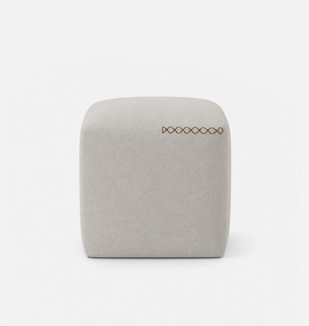 A square, low-profile pouf or ottoman upholstered in a light grey textured fabric, featuring leather x-stitching on the top surface, set against a seamless white background.