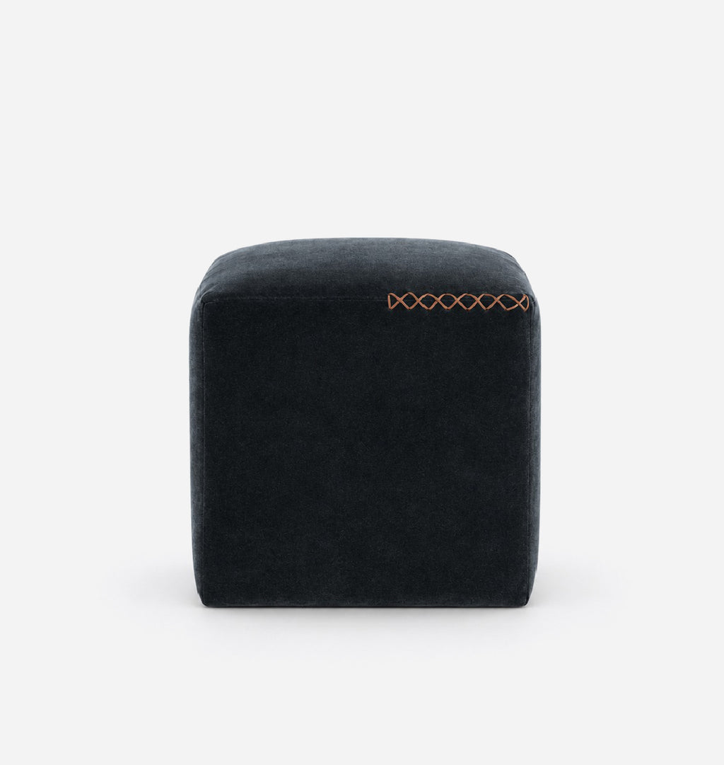 A dark navy blue velvet cube ottoman with a leather x-stitched accent on the top right, shown against a plain white background.