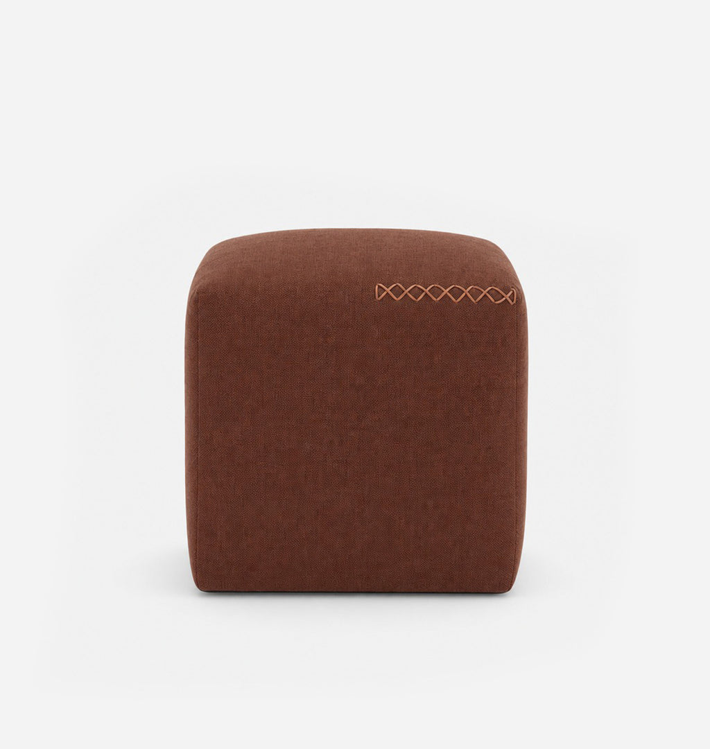 A square, low-profile pouf or ottoman upholstered in a red brown textured fabric, featuring leather x-stitching on the top surface, set against a seamless white background.