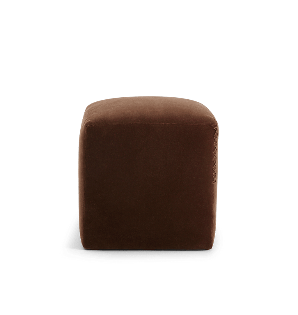 A square brown velvet ottoman with a leather x-stitched accent on the side edge, shown against a plain white background.