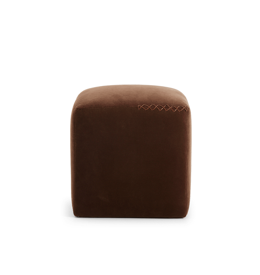 A square brown velvet ottoman with a leather x-stitched accent on the top edge, shown against a plain white background.