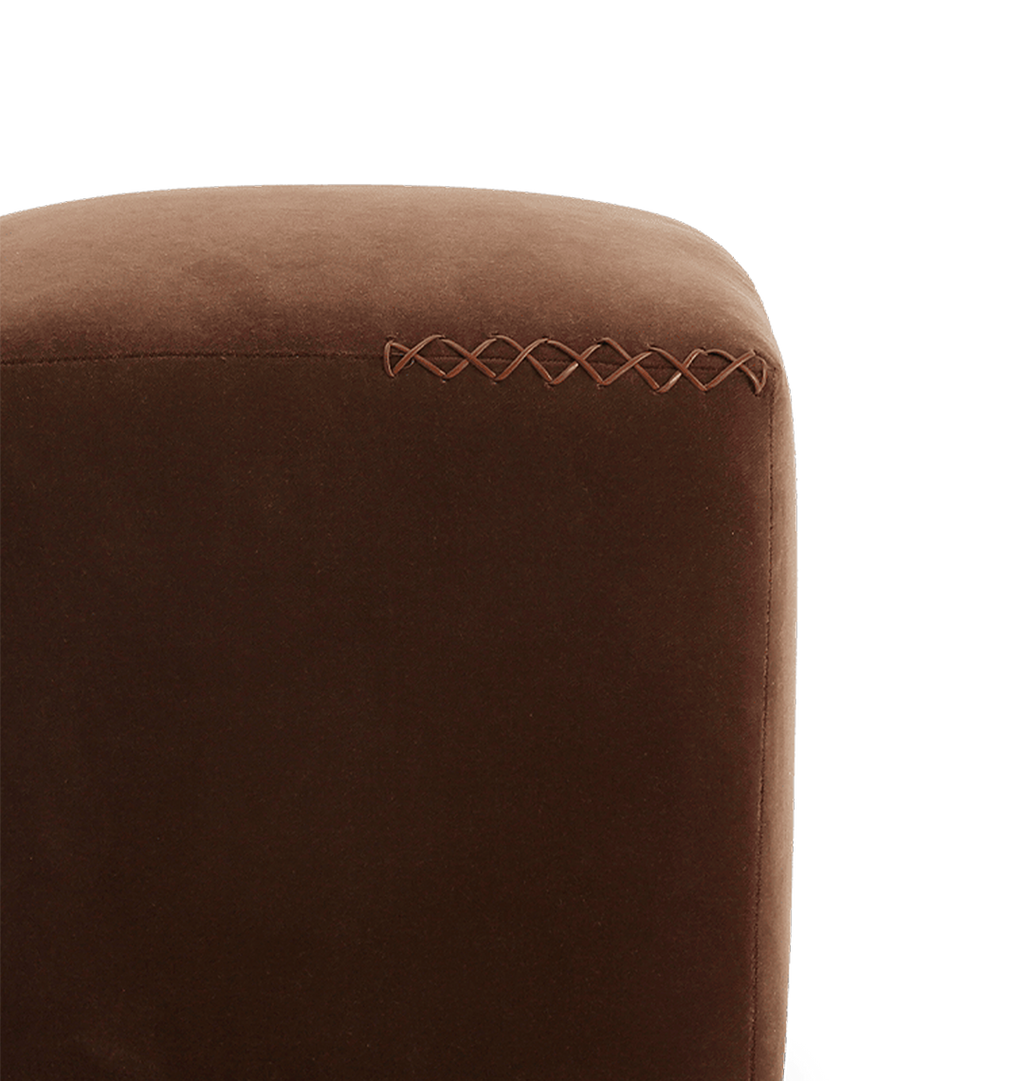 Close-up of a brown upholstered furniture corner with decorative x-stitched leather trim on a white background.