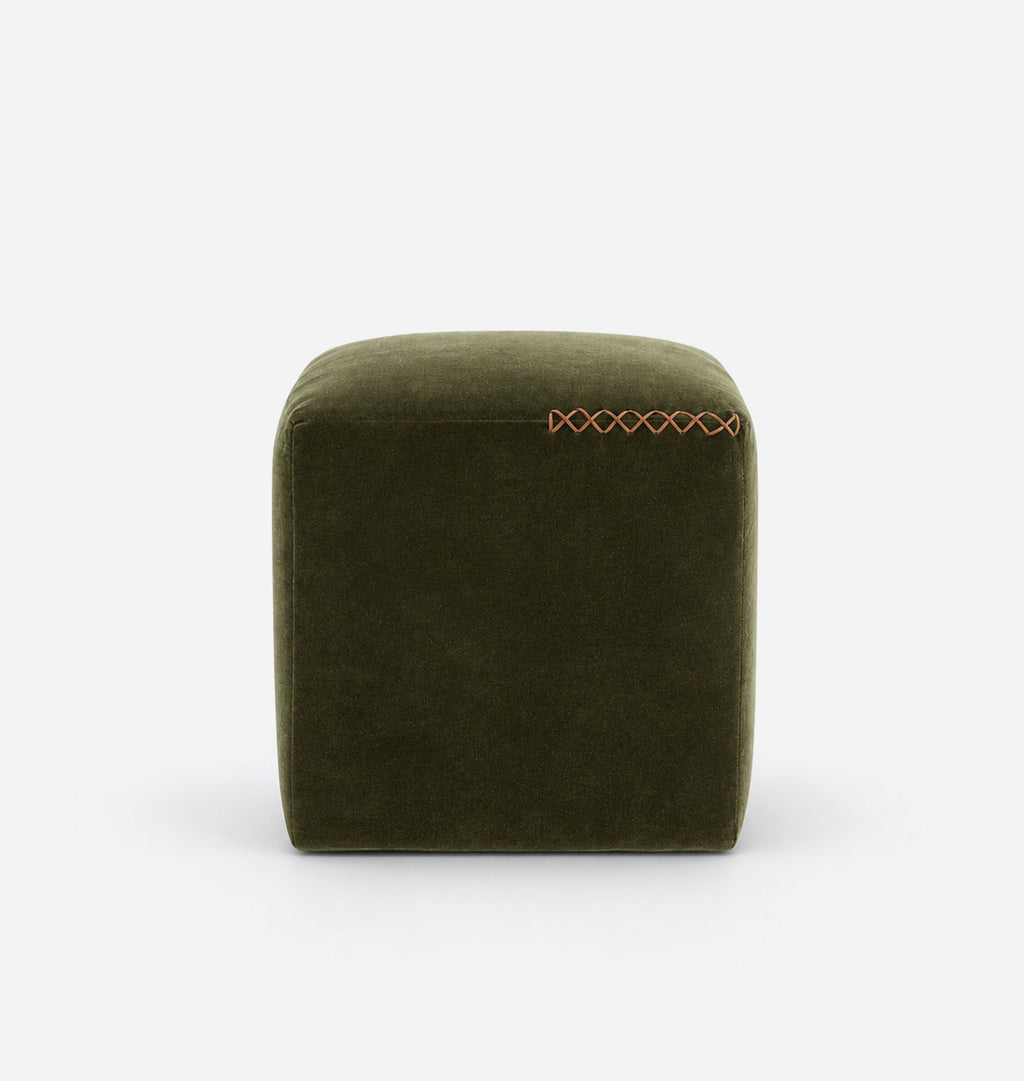 An olive green velvet cube ottoman with a leather x-stitched accent on the top right, shown against a plain white background.