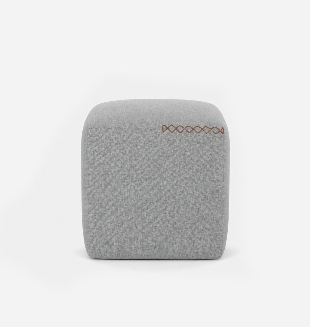 A square, low-profile pouf or ottoman upholstered in a light blue grey textured fabric, featuring leather x-stitching on the top surface, set against a seamless white background.