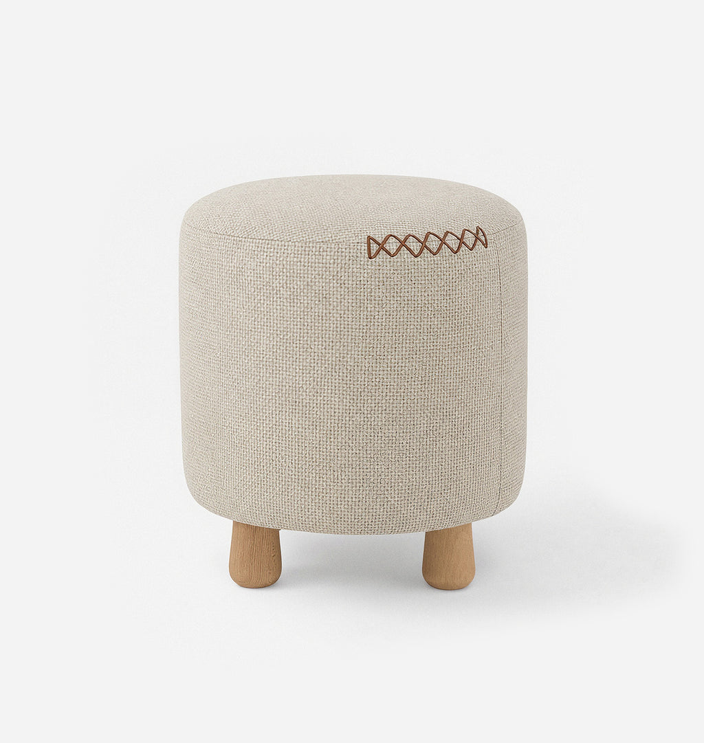 A round upholstered ottoman stool with a light beige textured woven fabric with leather x-stitching and three short natural wood legs, shown against a plain white background.