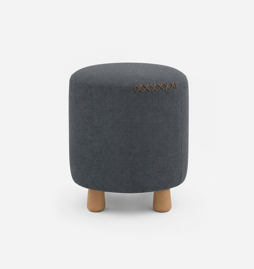 A round upholstered ottoman stool with a dark blue grey textured linen fabric with leather x-stitching and three short natural wood legs, shown against a plain white background.