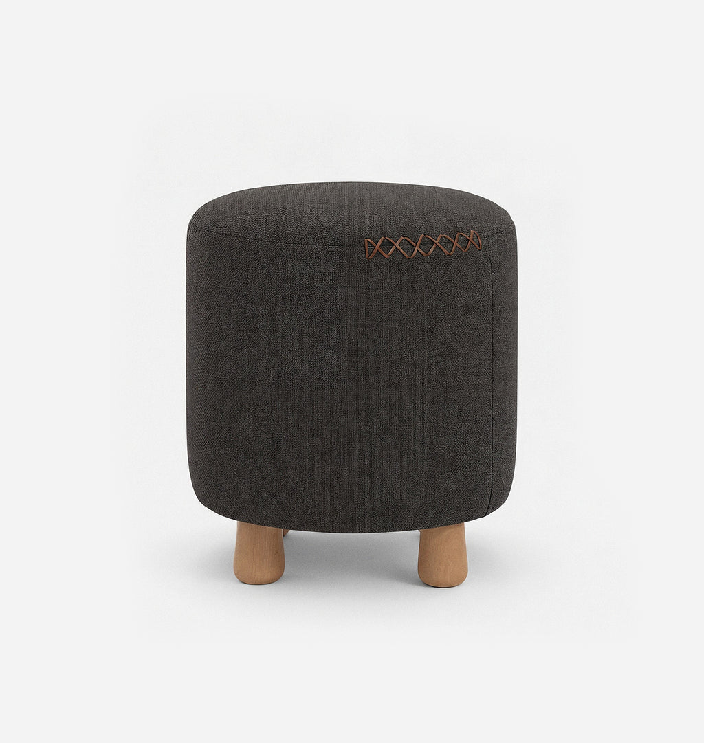 A round upholstered ottoman stool with a dark brown textured linen fabric with leather x-stitching and three short natural wood legs, shown against a plain white background.