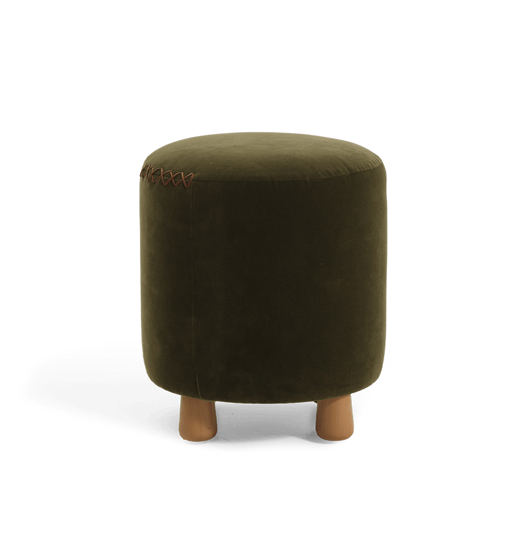 An olive green velvet cylindrical ottoman with short wooden legs and a decorative leather x-stitching on the top seam, shown against a plain white background.