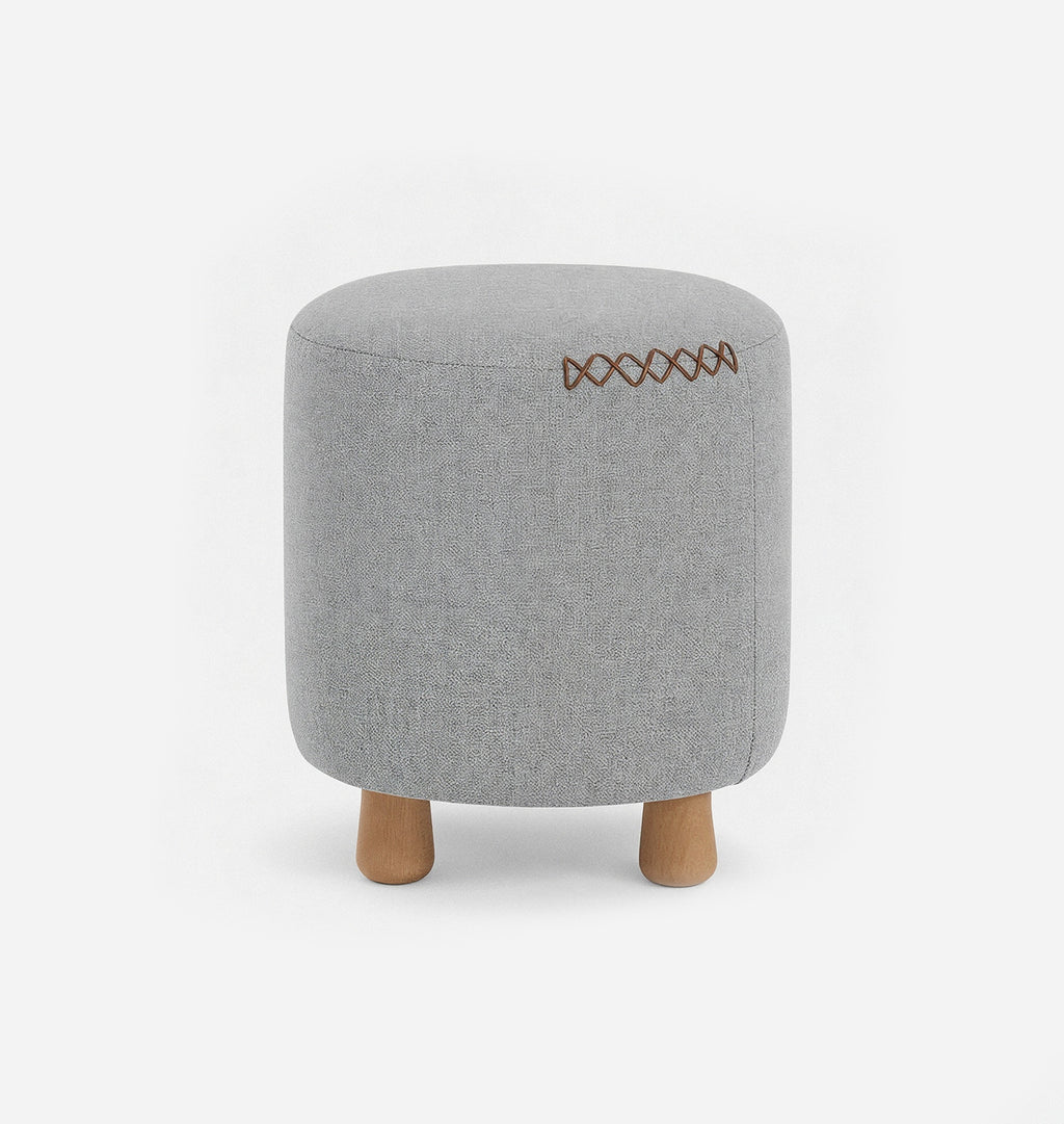 A round upholstered ottoman stool with a blue grey textured linen fabric with leather x-stitching and three short natural wood legs, shown against a plain white background.