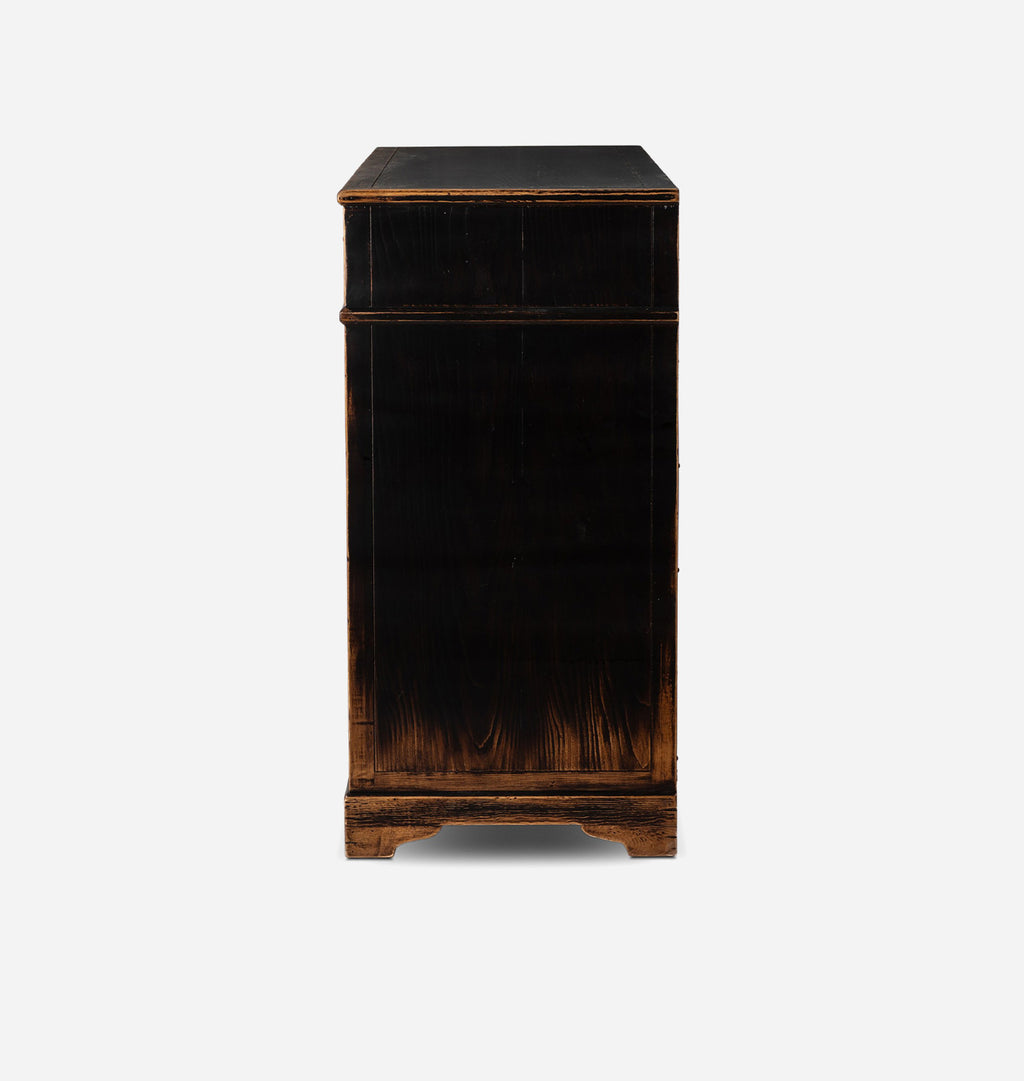 A tall, narrow black wooden cabinet or chest with a distressed finish showing warm brown wood grain underneath, photographed against a plain light gray background.