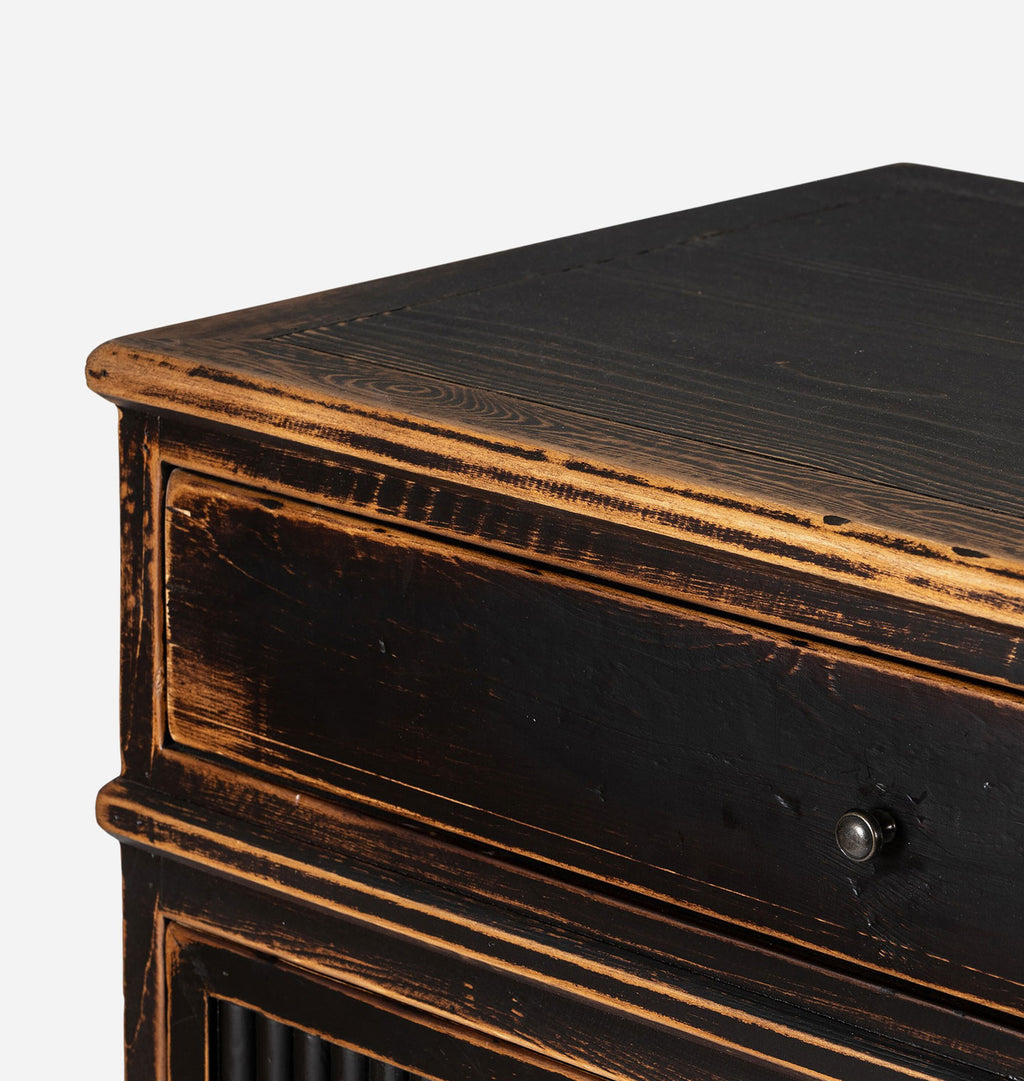 Close-up of a distressed dark brown wooden cabinet corner showing the top surface, drawer front, and part of the lower cabinet door with a glass panel.