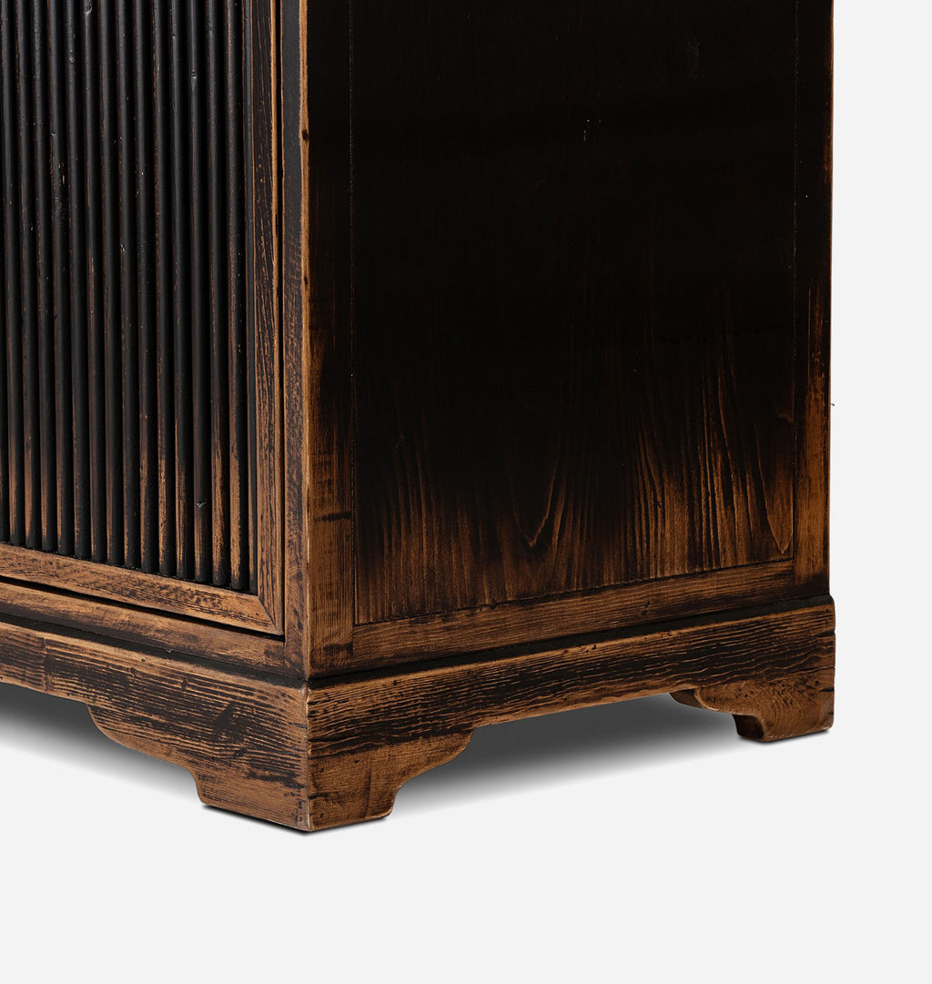 Close-up detail of a dark brown wooden cabinet or storage unit, showing the side panel, vertical slatted front, and carved feet on a light gray background.