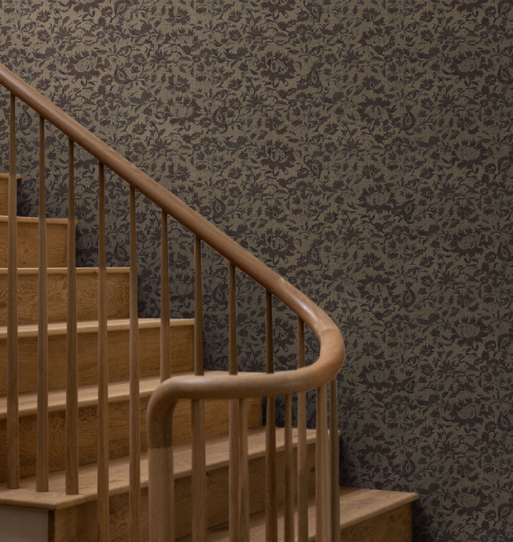 Damask patterned Raffi Grasscloth Wallpaper in dark brown and gray tones shown on a wall behind a wooden staircase with a curved handrail.
