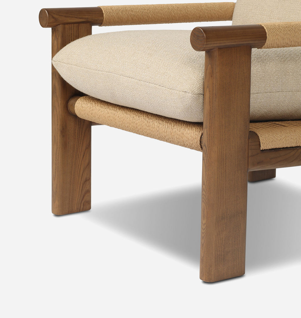 Close-up of a wooden armchair showing the lower front section, with a medium brown wood frame, woven natural-fiber seat and arm accents, and a light beige upholstered cushion on a white background.