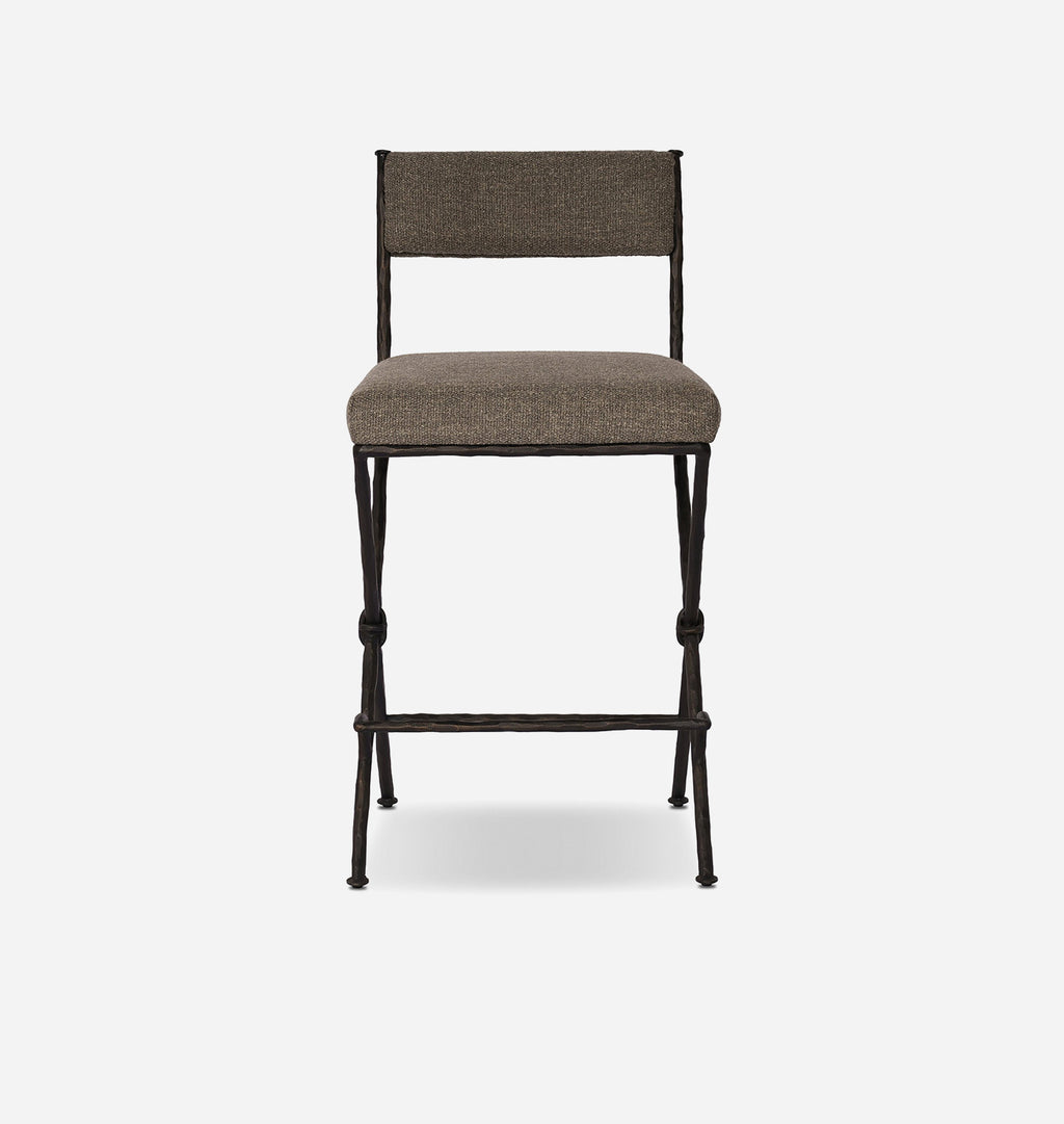 A modern counter stool with a textured taupe-brown upholstered seat and backrest, supported by a dark metal frame with knolled legs and a footrest, shown against a light gray background.