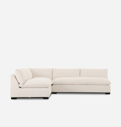 A modern sectional sofa upholstered in a light cream fabric, featuring a lchaise lounge and a low rectangular seat, shown against a plain white background.