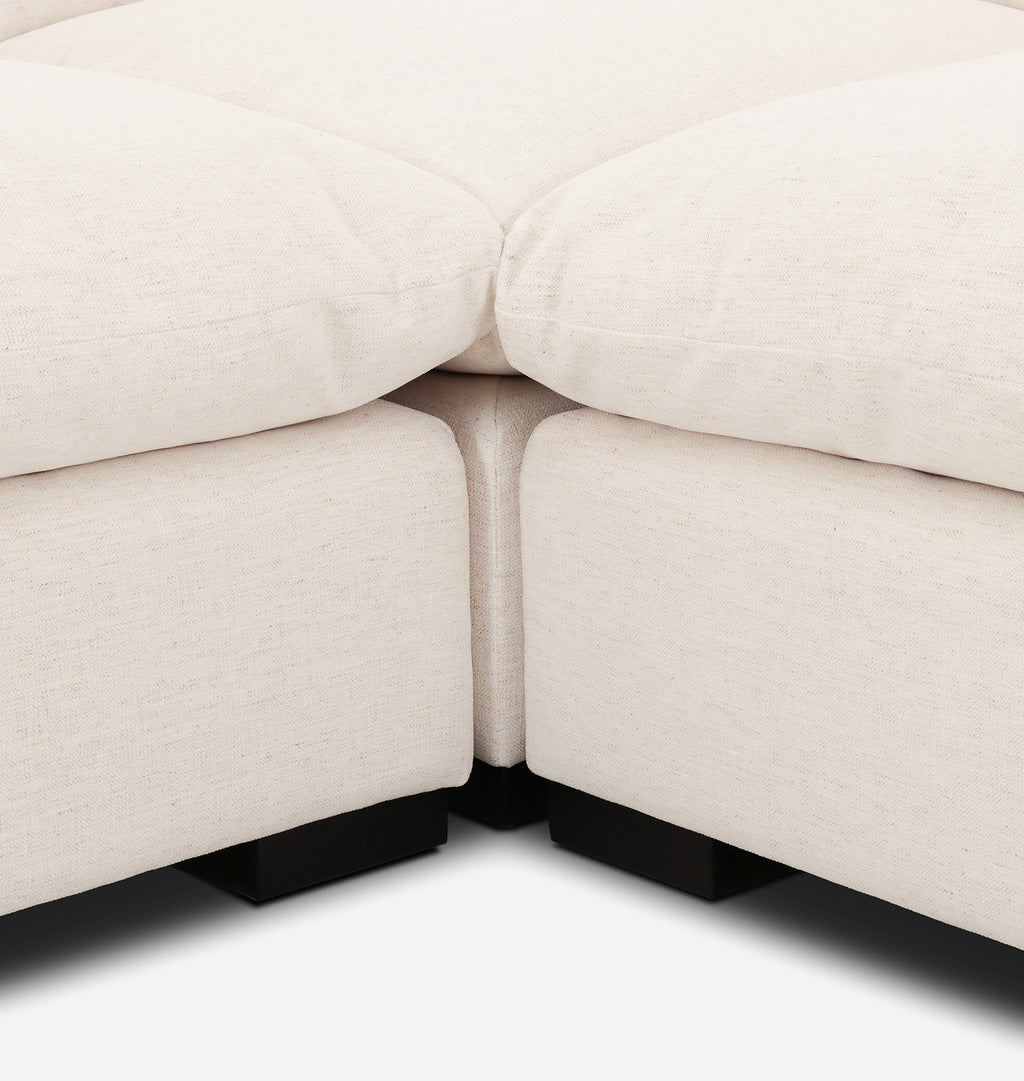 Close-up of a light beige upholstered sectional sofa corner with dark square feet visible against a white background.
