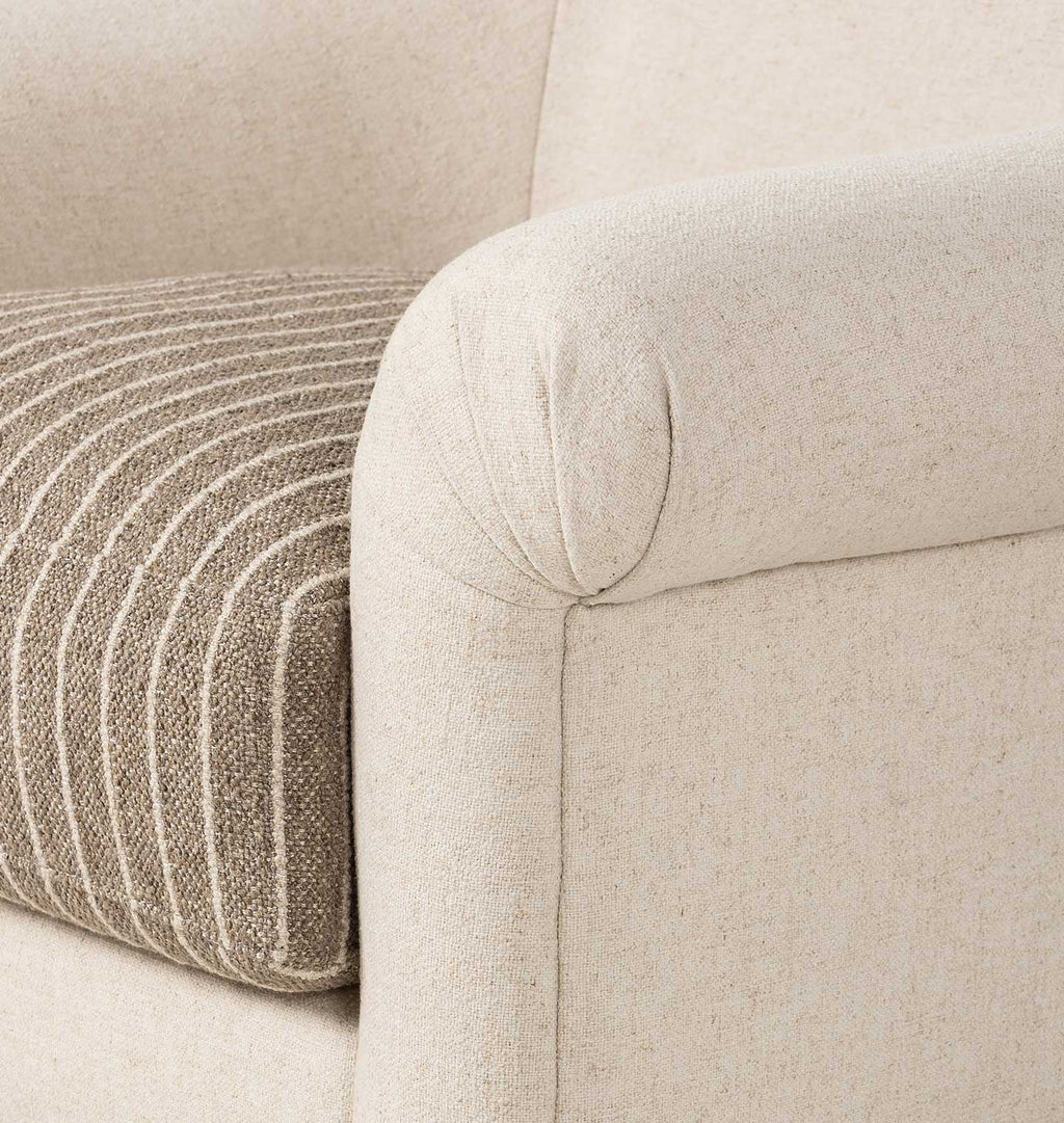 Close-up of a cream-colored upholstered sofa arm with a textured striped throw pillow in beige and taupe.