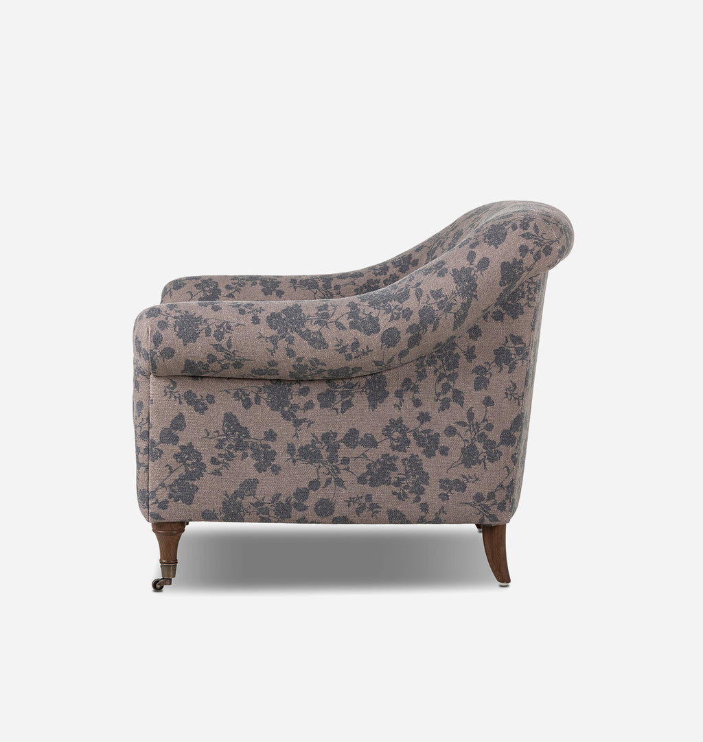 A vintage-style upholstered armchair with a dusty pink floral pattern and dark brown wooden legs, shown from a side view against a light gray background.