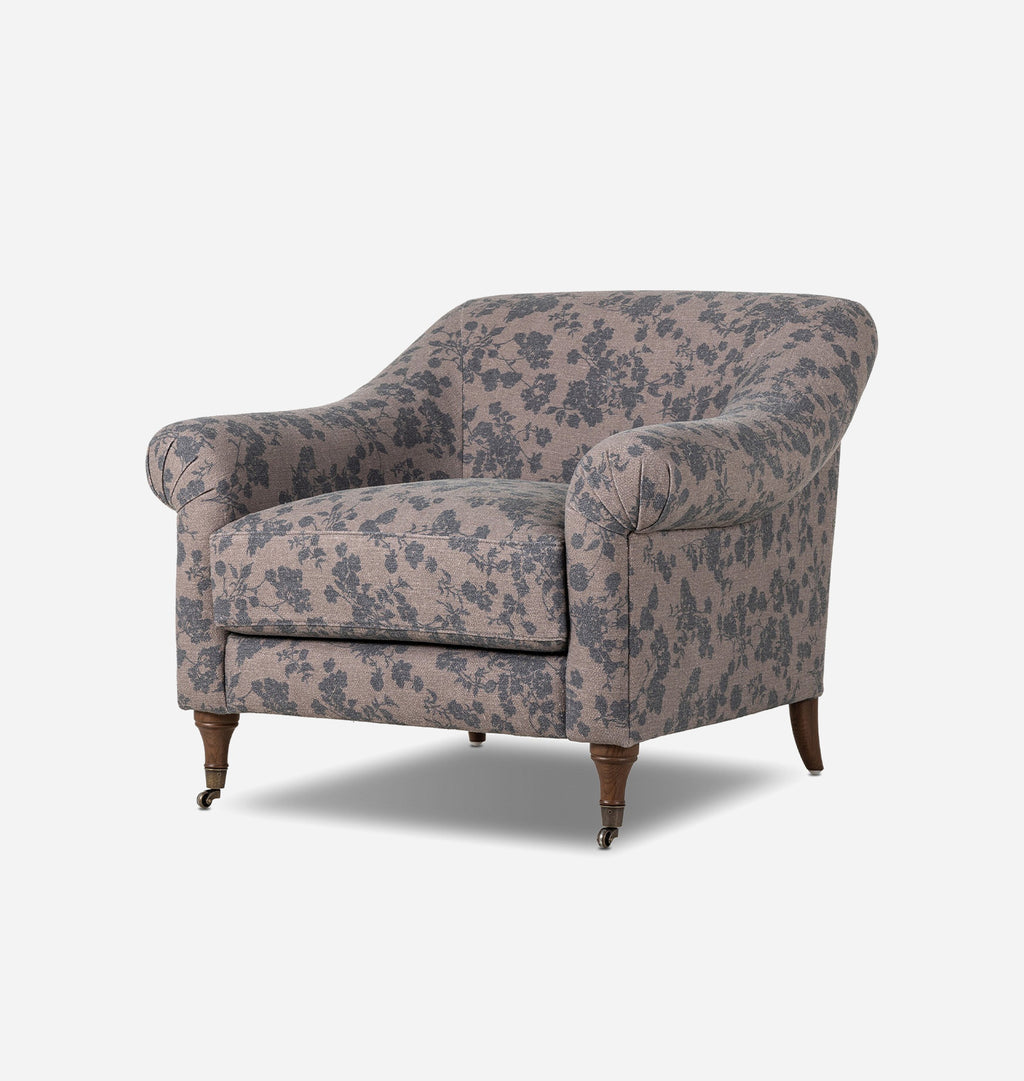 A vintage-style upholstered armchair with a dusty pink floral pattern and dark brown wooden legs, shown from a three-quarters angle against a light gray background.