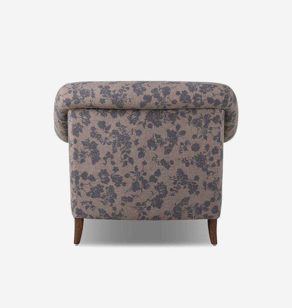 A vintage-style upholstered armchair with a dusty pink floral pattern and dark brown wooden legs, shown from a back angle against a light gray background.