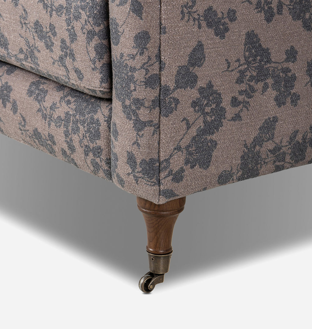 A close up of a vintage-style upholstered armchair with a dusty pink floral pattern and dark brown wooden legs against a light gray background.