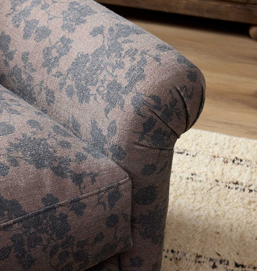 A close up of a vintage-style upholstered armchair with a dusty pink floral pattern chair arm