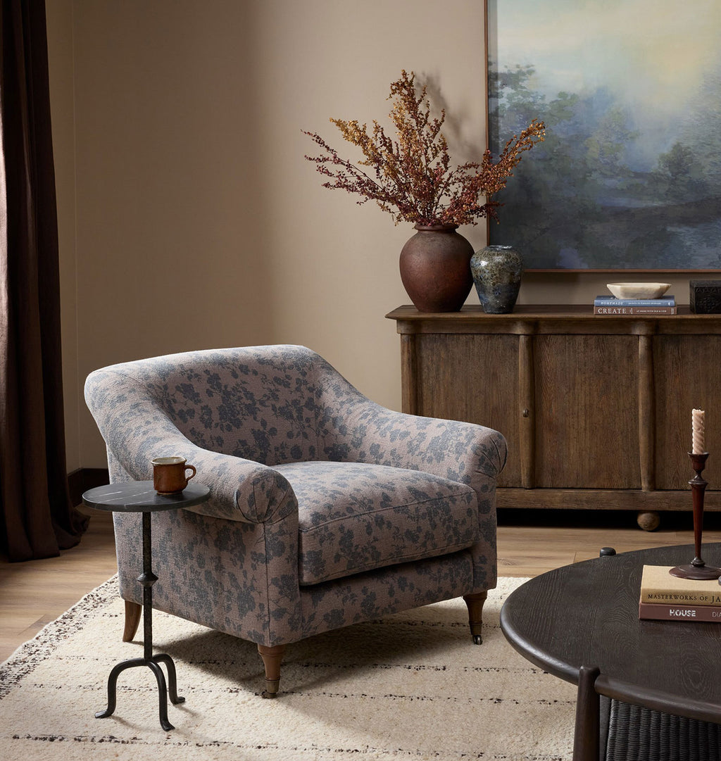 A vintage-style upholstered armchair with a dusty pink floral pattern and dark brown wooden legs, shown from a three-quarters angle against living room scene