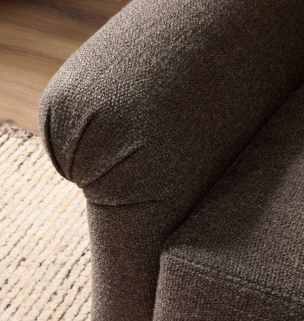 Close-up of a textured upholstered armrest in a warm taupe-brown fabric, showing the fabric weave and rounded arm detail in an indoor setting.