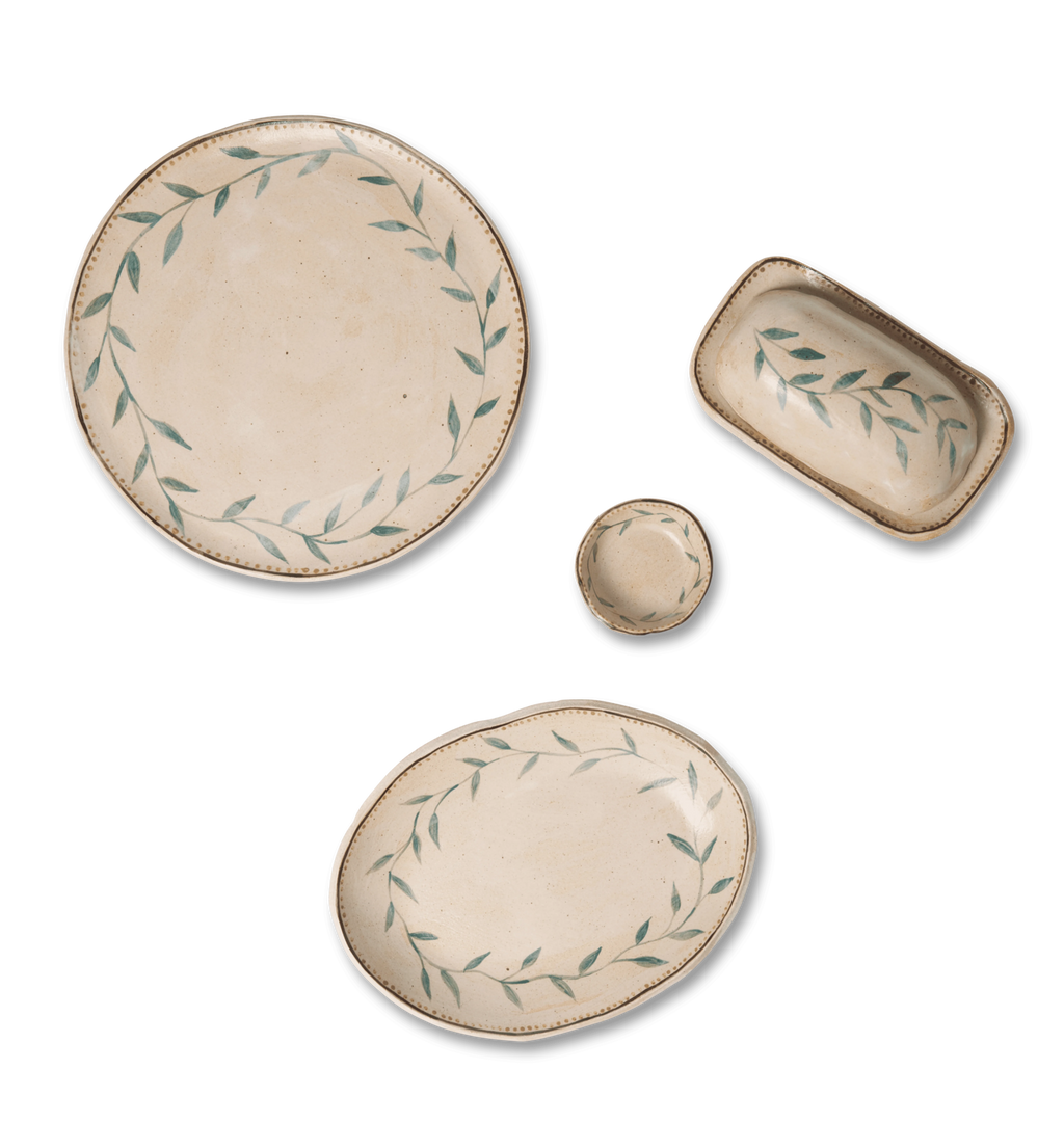 Group shot of ceramic serving plates, a salt dish, and a matching butter dish decorated with a green leafy vine border and a gold dotted accent line on a white background
