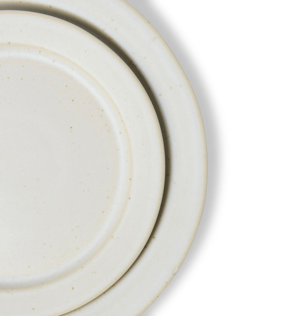 A close up detail shot of a round ceramic salad and dinner plate in an off white glaze shown on a white background