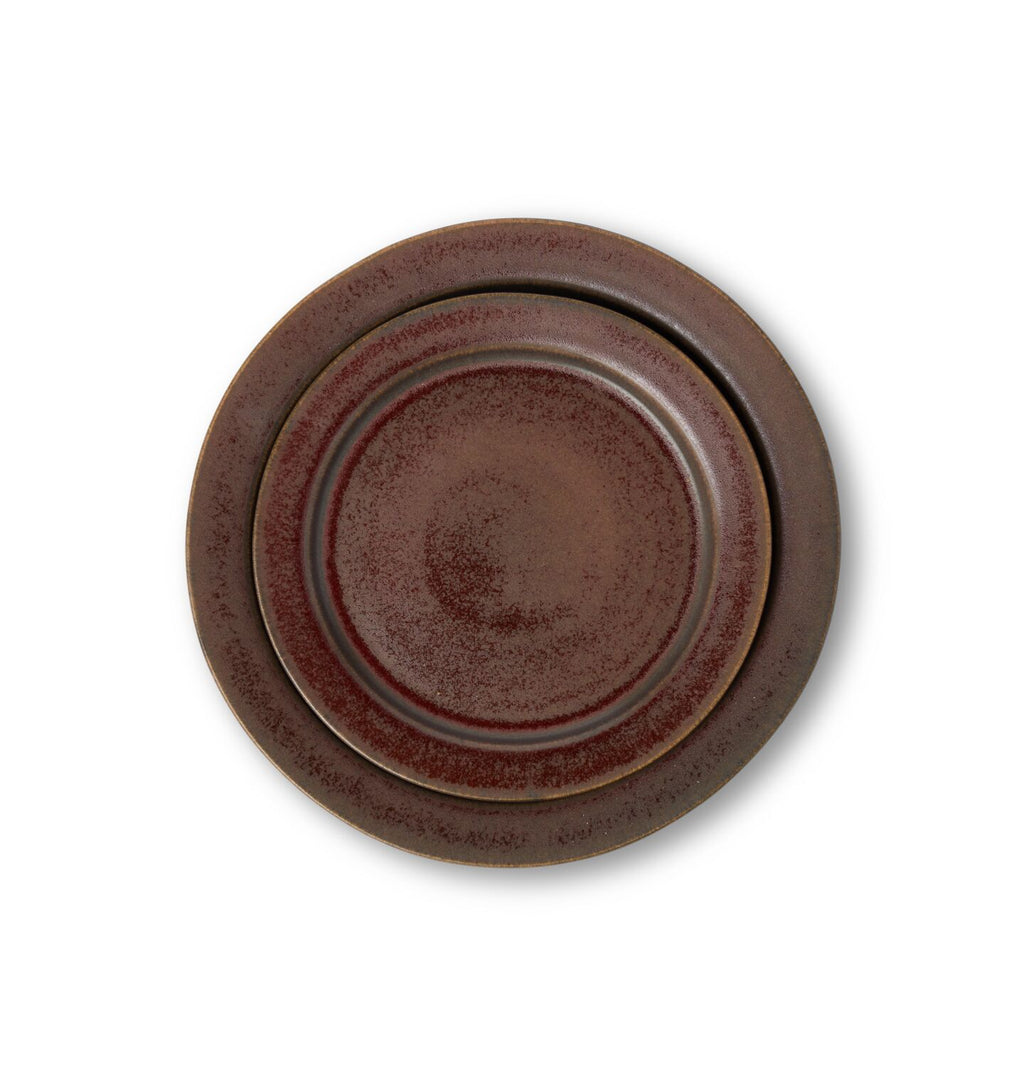 An overhead view of a ceramic salad and dinner plate finished in a reddish brown glaze shown on a white background